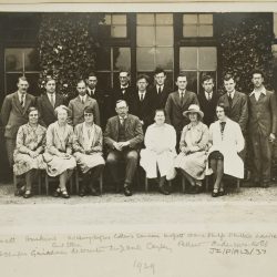 A black and white photo from the 1920s of men in suits standing up with women sitting down